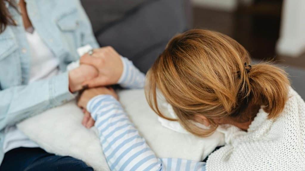 A woman rests her head on a pillow while holding someone’s hands for comfort.