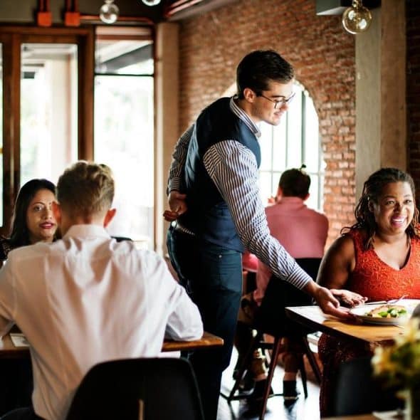 A waiter serving food to diners in a busy restaurant.