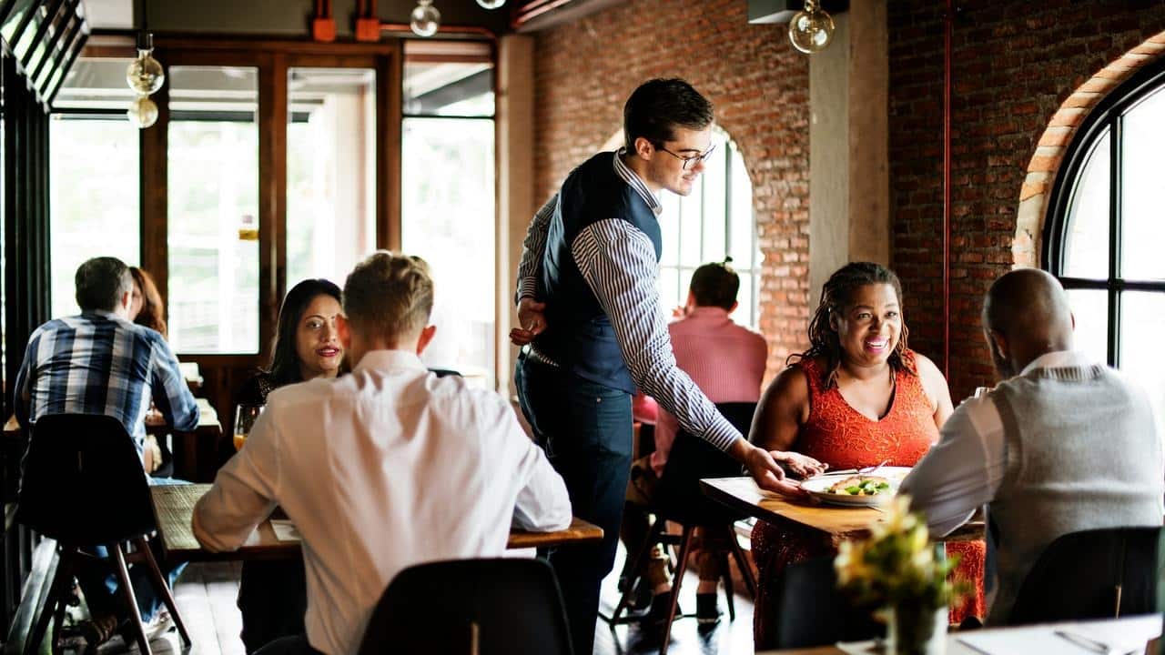 A waiter serving food to diners in a busy restaurant.