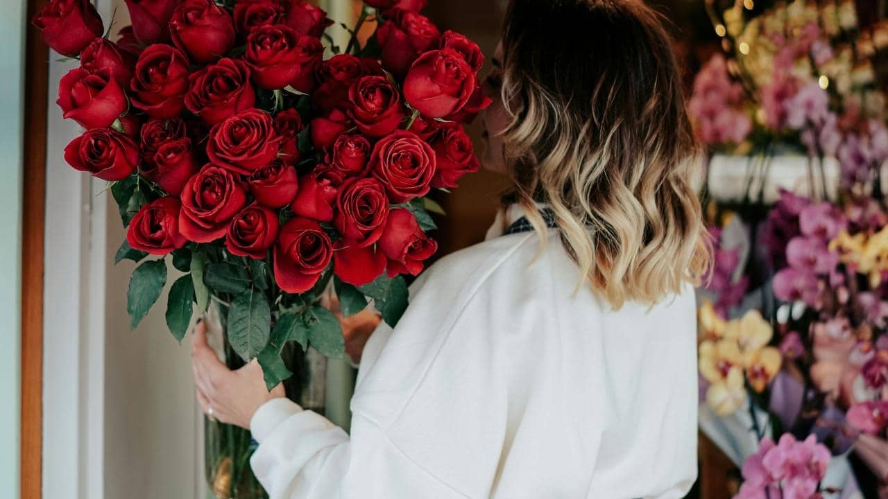A woman holding a large bouquet of red roses in a flower shop.