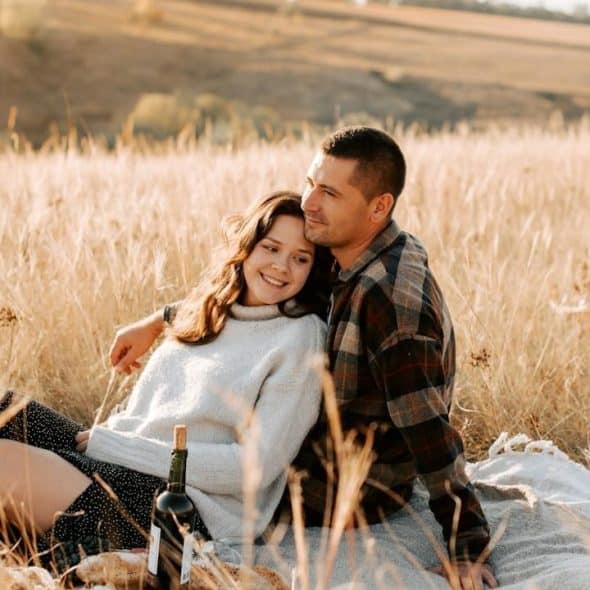 A woman leaning her husband while they are sitting together in a field.