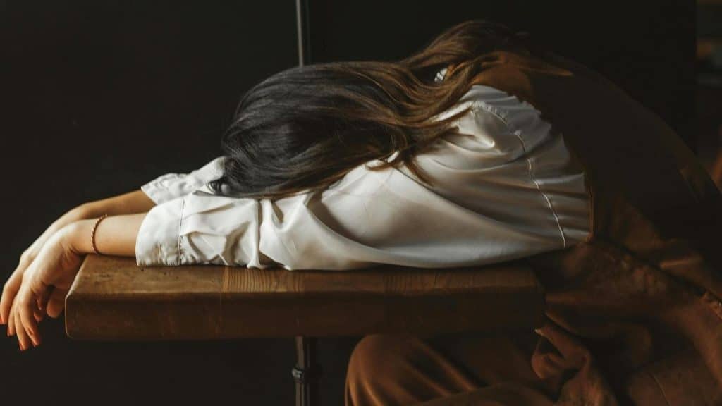 A woman resting her head on a table with her arms outstretched.