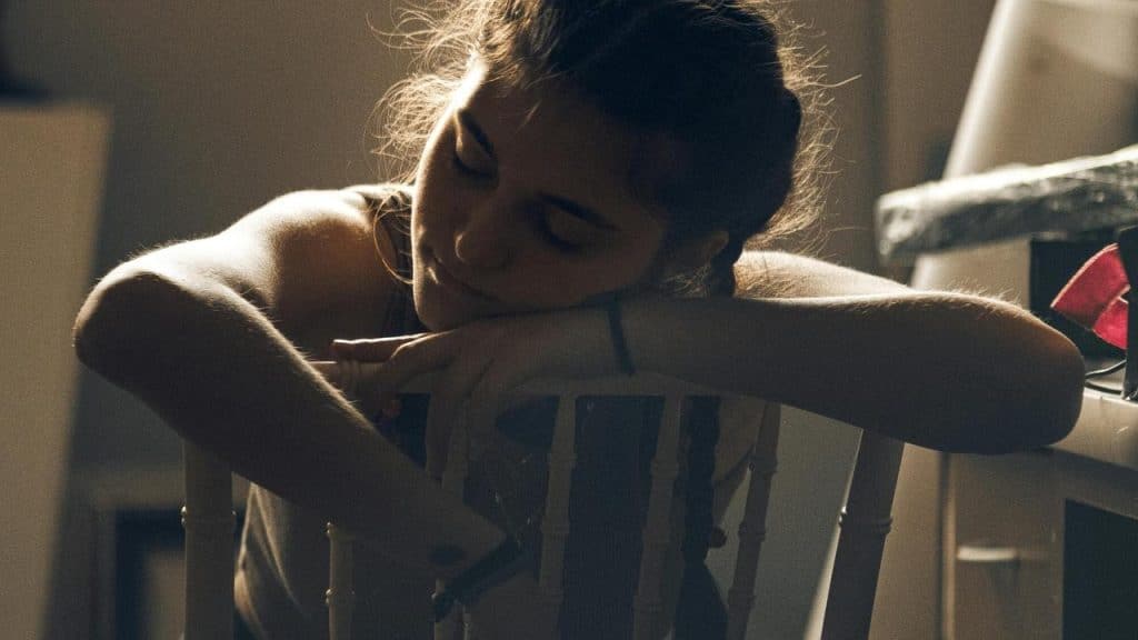 A tired woman resting her head on her arms over a chair.