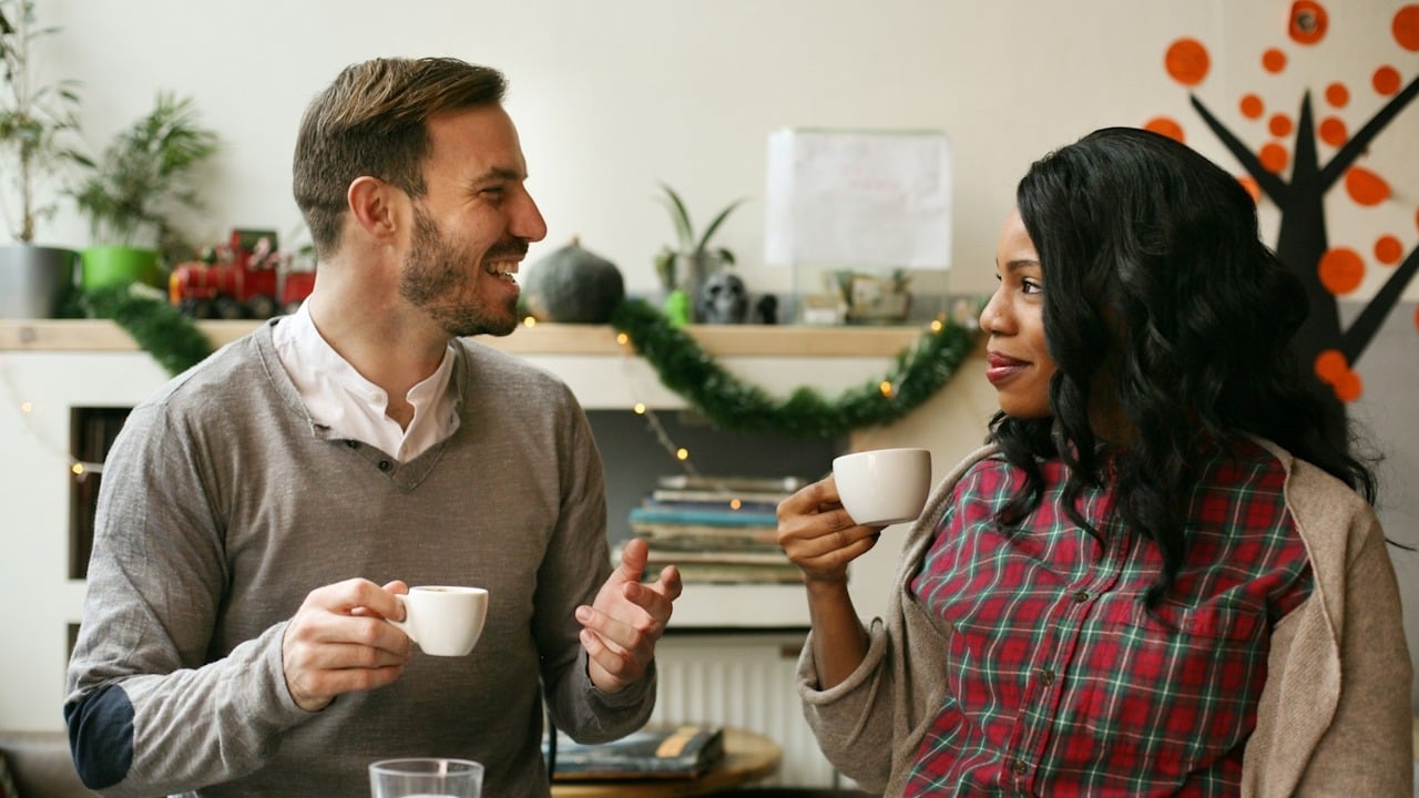 A couple smiling at each other while talking and having coffee in a cafe.