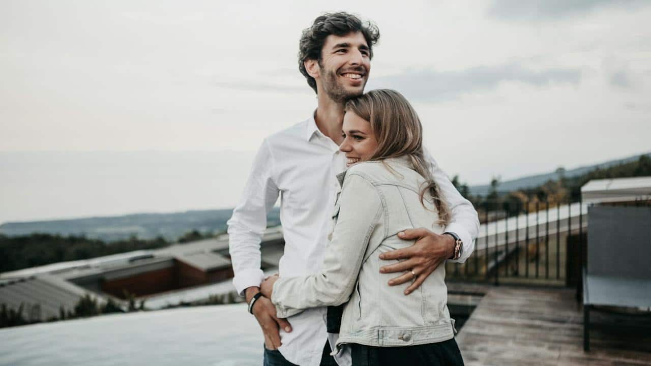 A man hugging his wife in a happy mood while they are standing outdoors.