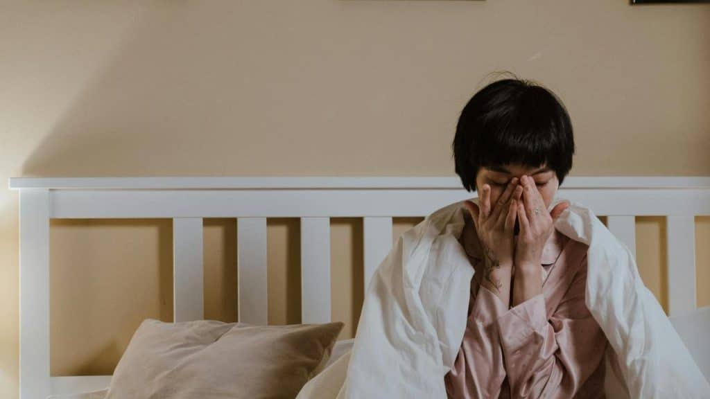 A person sitting in bed with hands covering their face.