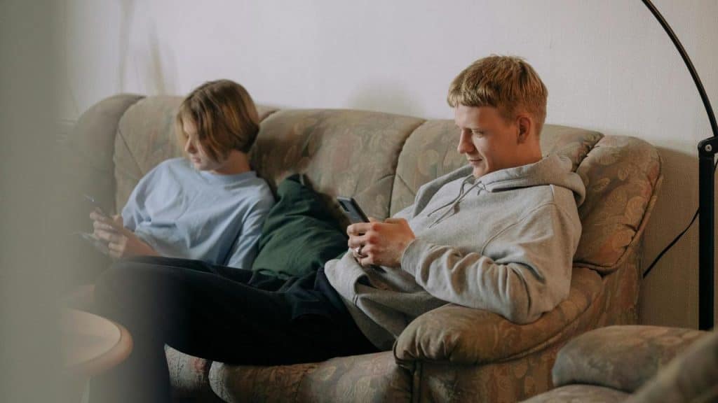 A couple sitting on a couch while looking at their phones.