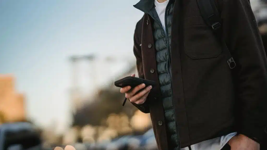 A person holding a smartphone while standing outdoors.