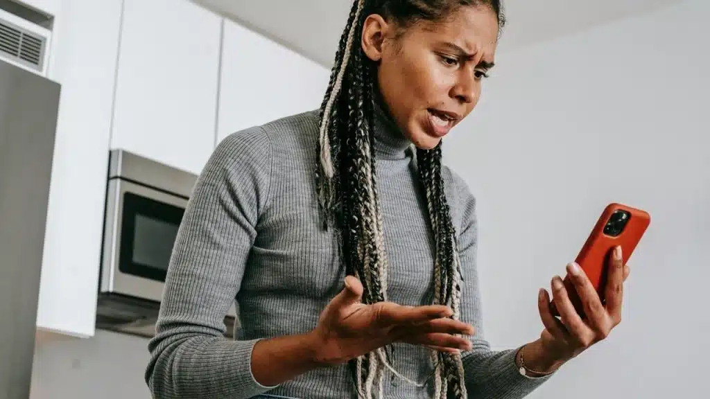 A woman looking frustrated while holding a smartphone indoors.