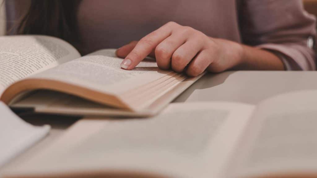 A person reading an open book and pointing at the text.