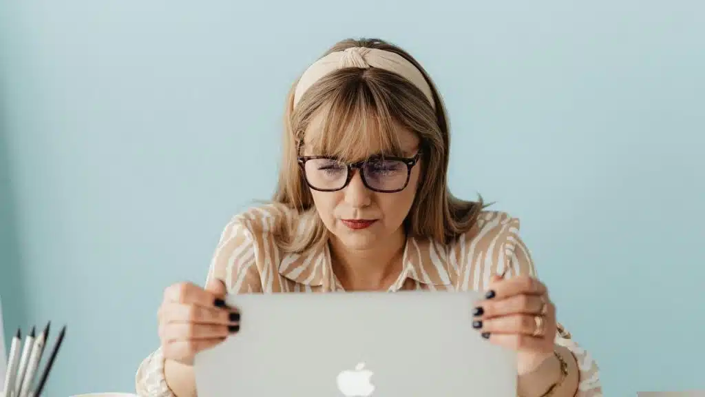 A woman wearing glasses looking closely at a laptop screen.
