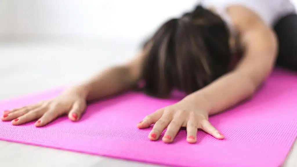 A person stretching forward on a pink yoga mat.