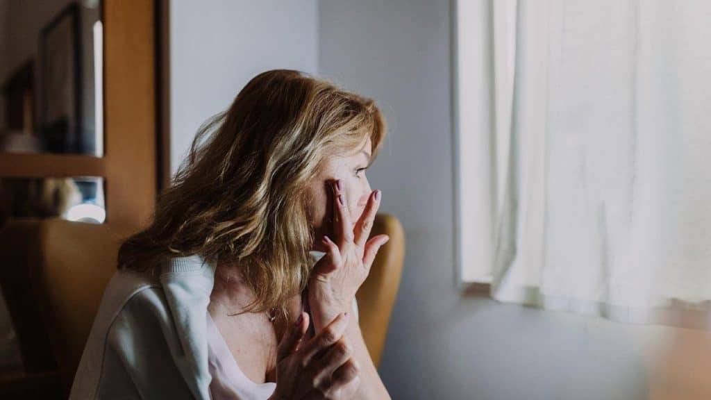 A woman looking out a window with her hand covering her mouth.