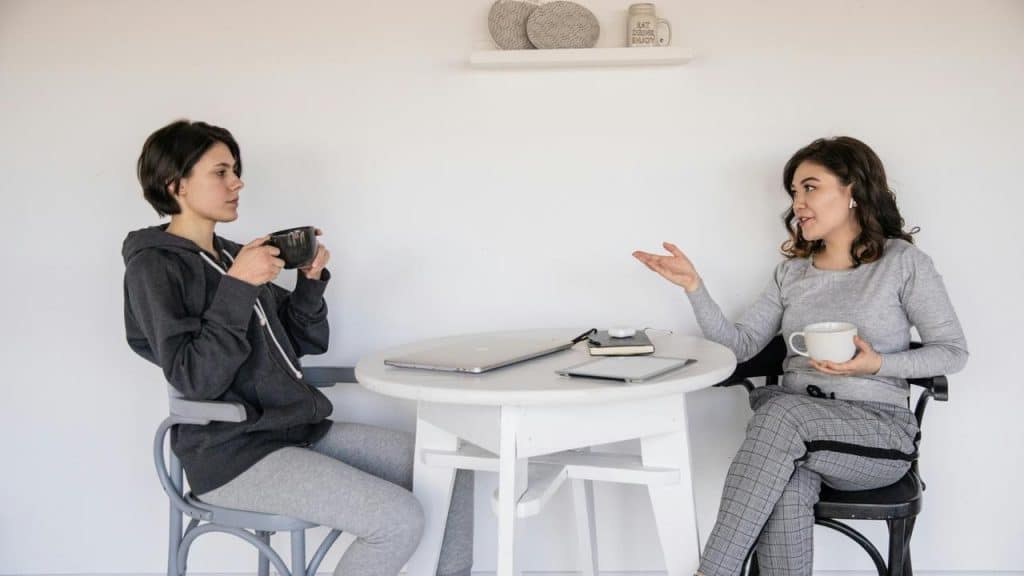 A woman talking with another woman over coffee at a table.
