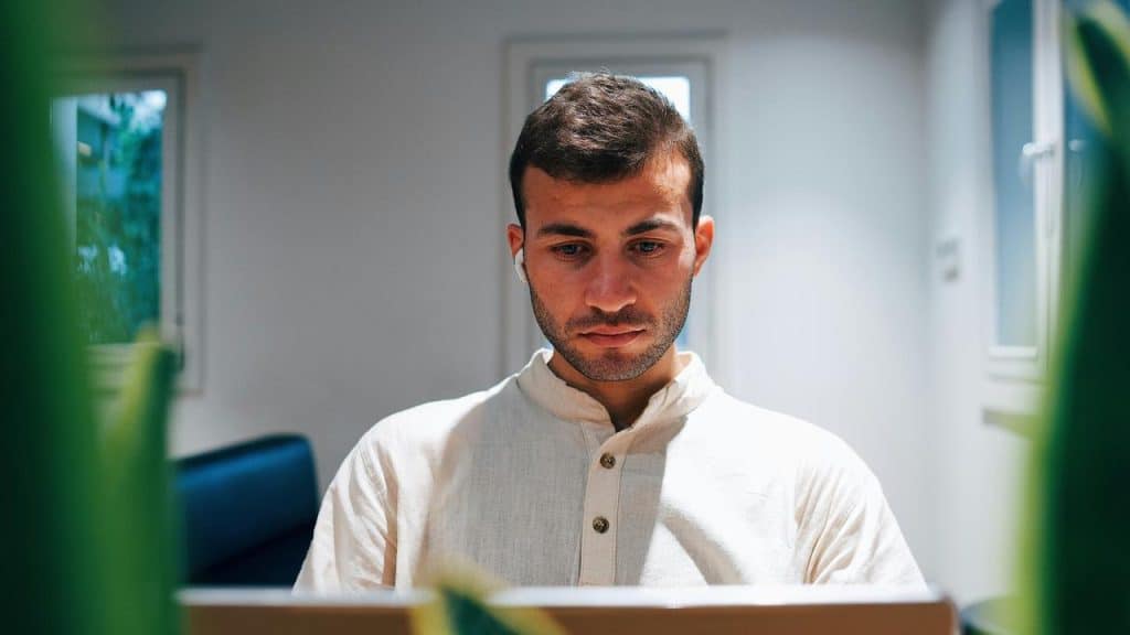 A focused man working on a laptop in a bright room.