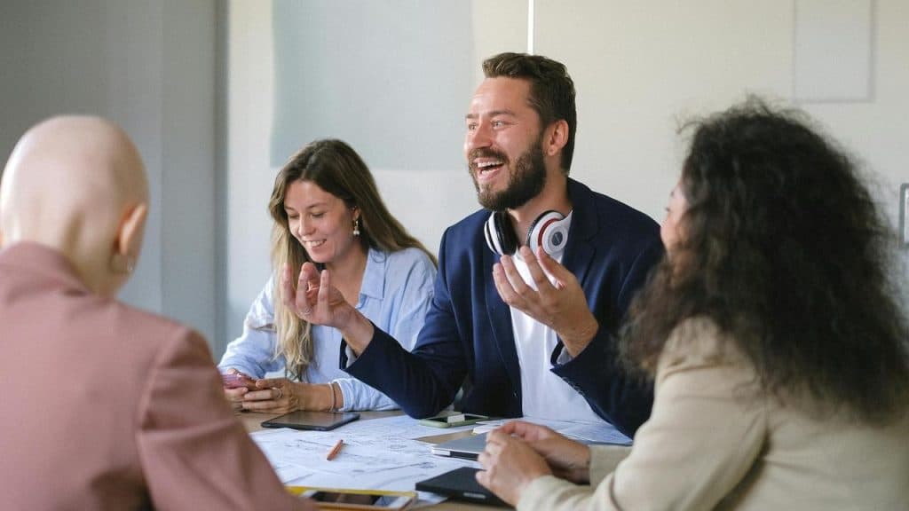 A group of coworkers laughing and talking during a meeting around a table.