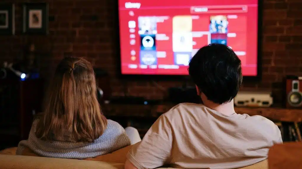 A couple sitting on a couch watching TV in a cozy living room.