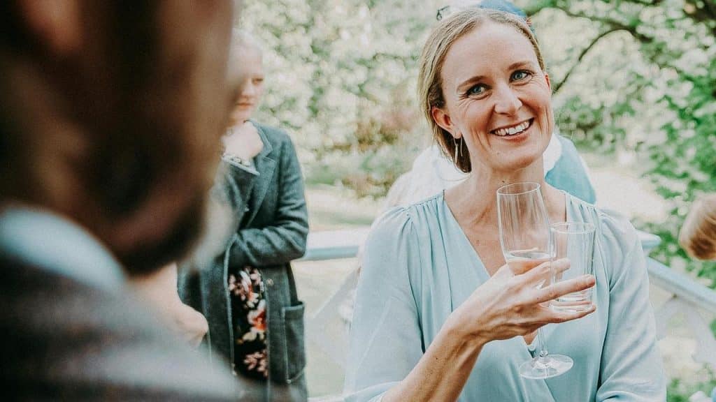A smiling woman holding a glass of champagne at an outdoor gathering.