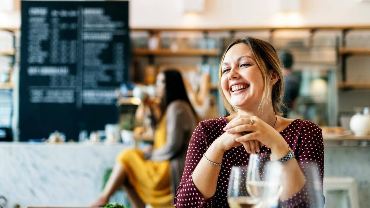 A smiling woman sitting at a café table with drinks.