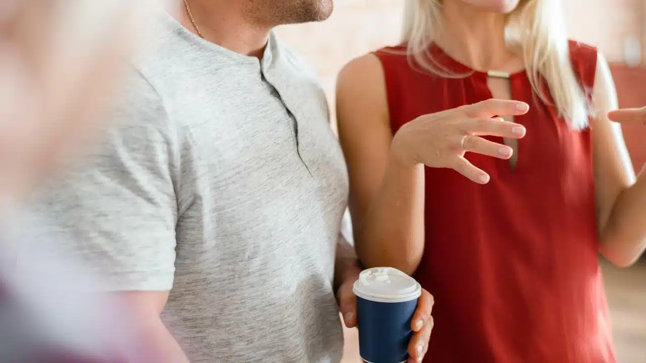 A man and woman chatting while holding takeaway coffee cups.