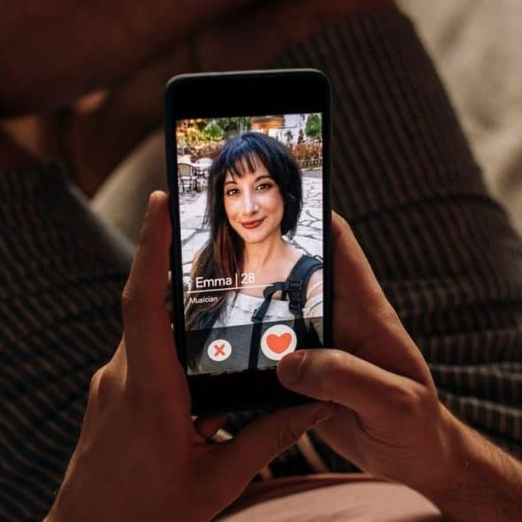 A person's hands hold a smartphone displaying a dating profile of a woman named Emma.