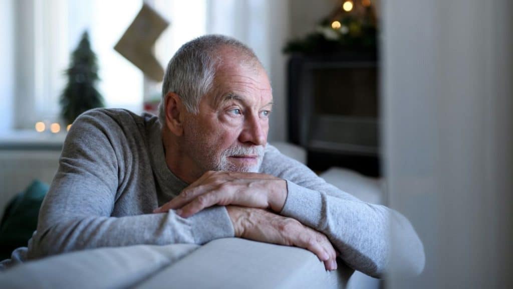 A gray-haired man rests his chin on his hands while looking thoughtfully out a window.