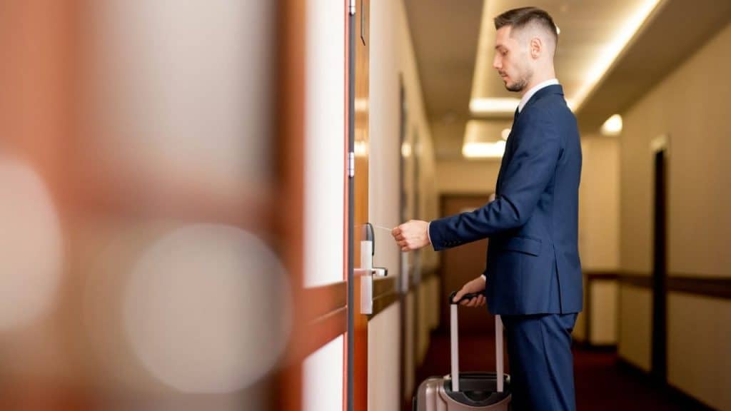 A man in a suit standing at the door in a long hallway.