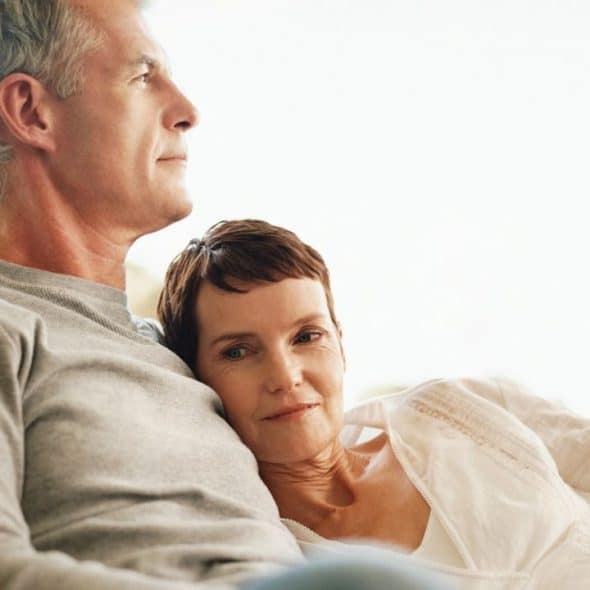 A man with gray hair and a woman resting her head on his shoulder look outward.