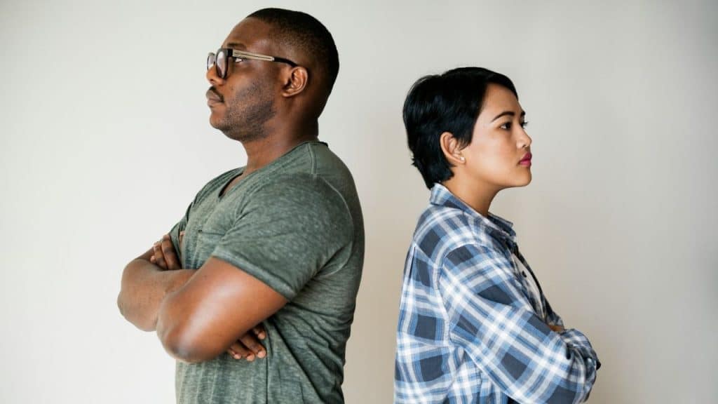 A man and woman stand back-to-back with their arms crossed against a plain white background.