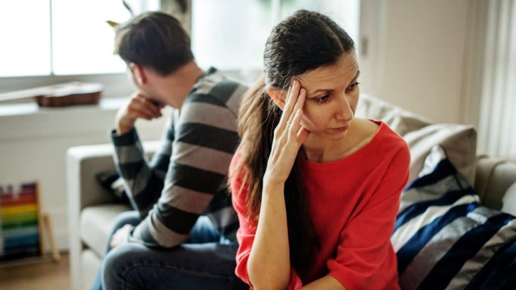 A woman in a red shirt rests her head on her hand while sitting.