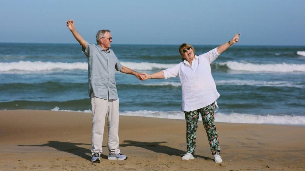 A man and woman hold hands and raise their arms while standing on a beach.