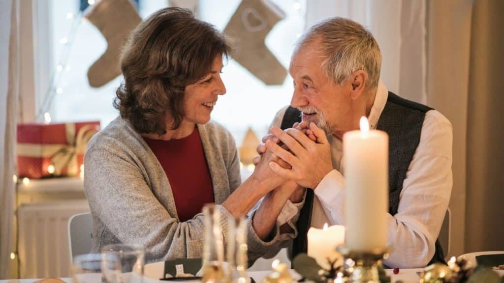 A man and woman sit at a candlelit table holding hands and smiling at each other.