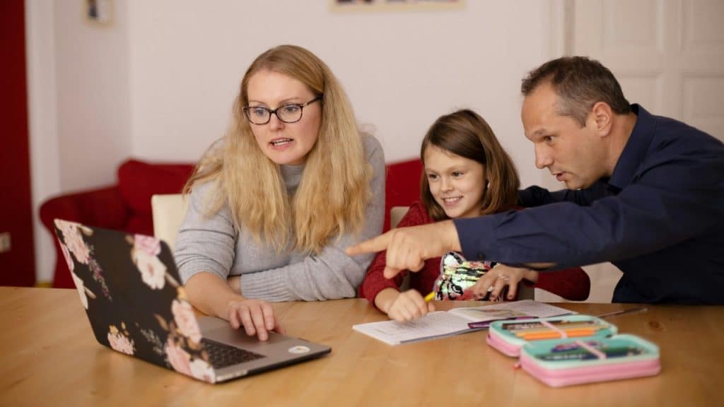 A man, woman, and young girl looking at a floral laptop on a wooden table.