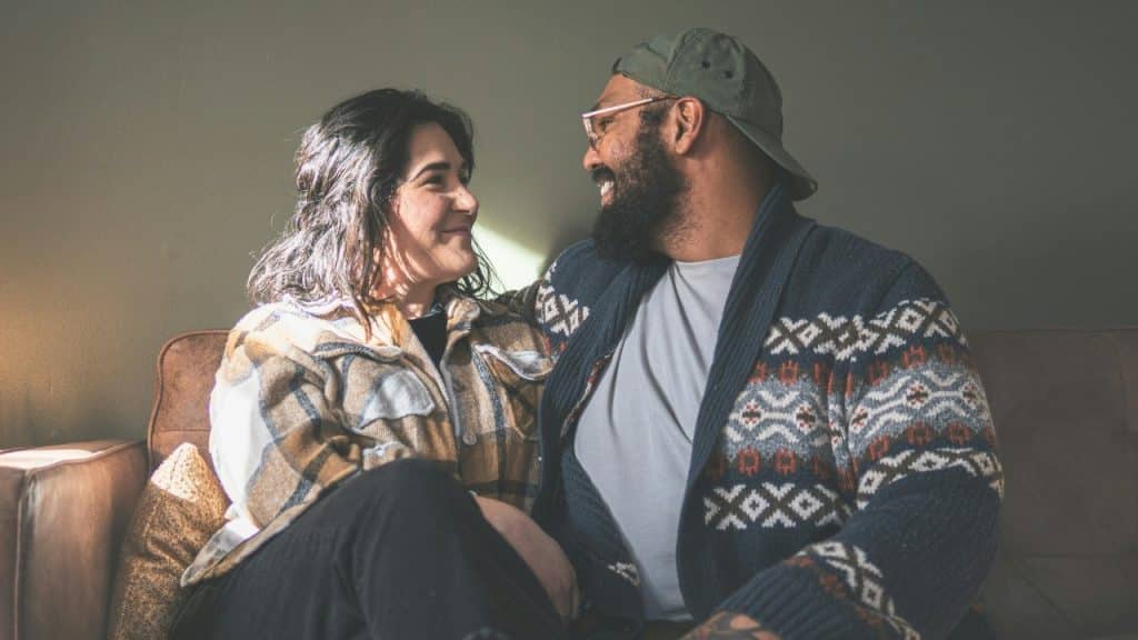 A man and woman sitting on a leather couch together, looking at each other smiling.