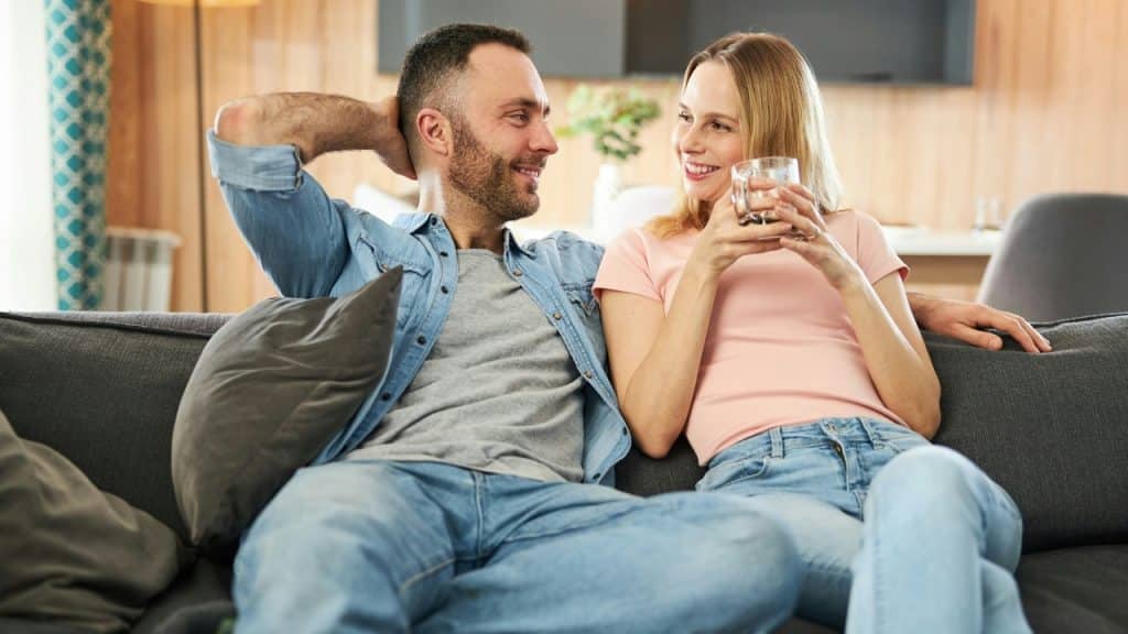 A man and woman sit on a sofa smiling and looking at each other.