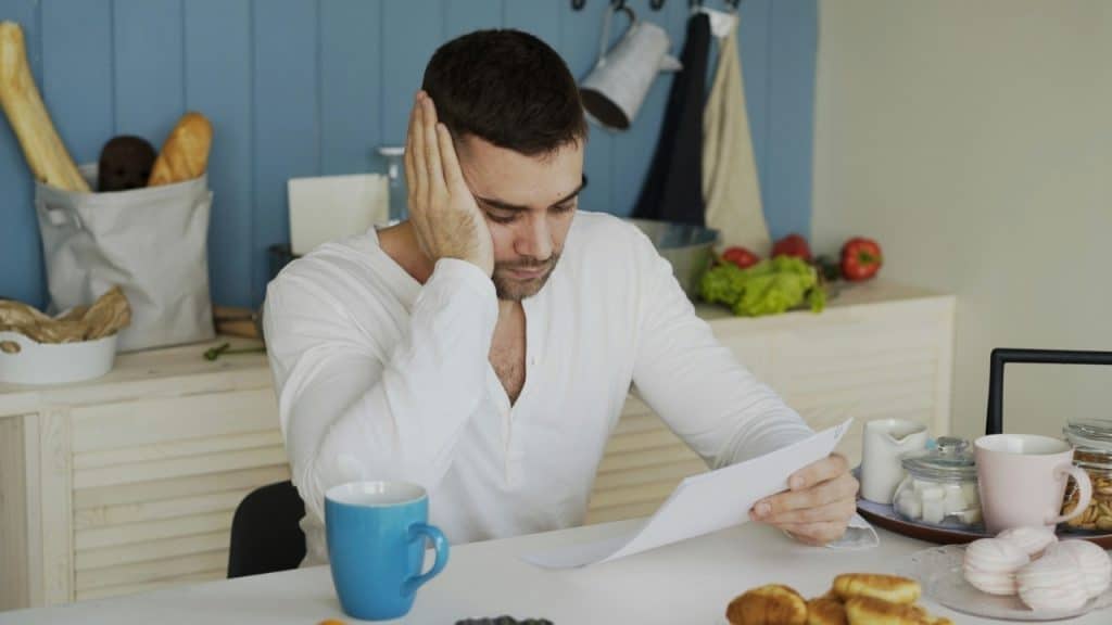 A man in a white shirt sits at a table looking down at a piece of white paper.