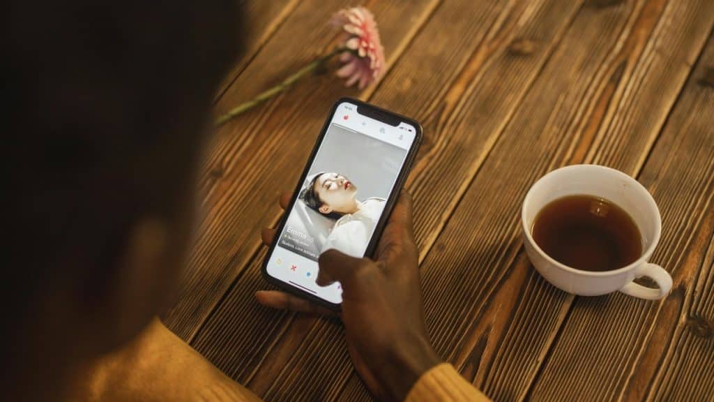 A hand holds a smartphone showing a dating profile next to a white cup of coffee.