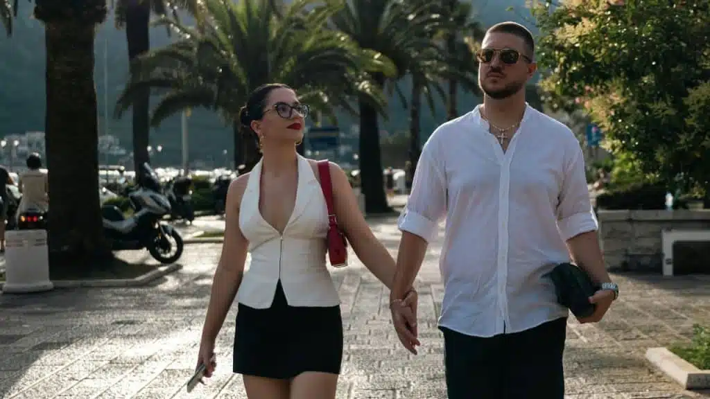 A man and woman walk outdoors on a paved path while holding hands during sunset.
