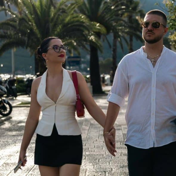 A man and woman walk outdoors on a paved path while holding hands during sunset.