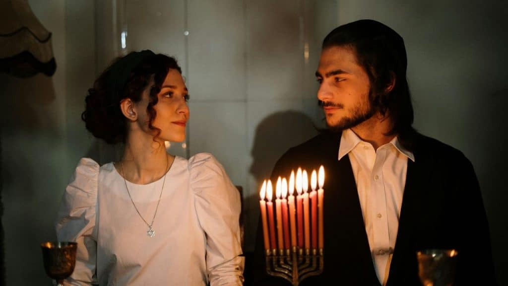 A man and woman look at each other behind a candelabra with several lit candles.