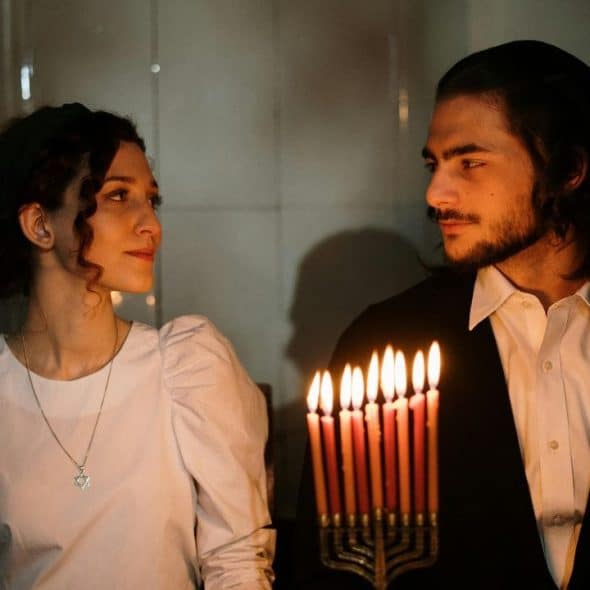 A man and woman look at each other behind a candelabra with several lit candles.