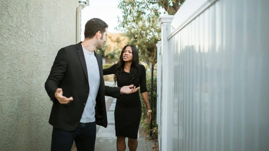 A man and woman gesture toward each other while standing on a narrow outdoor walkway.