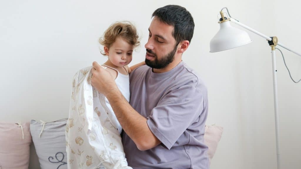 A man holding a young child and helping them put on a patterned white garment.