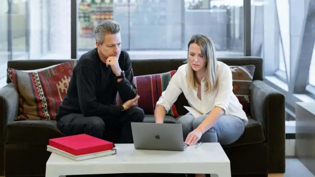 A man and woman sitting on a sofa looking at a laptop on a table.