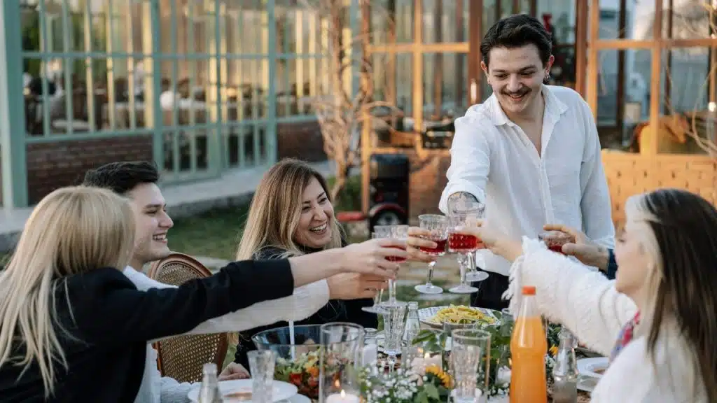 A group of people at an outdoor table raising their glasses together for a toast.
