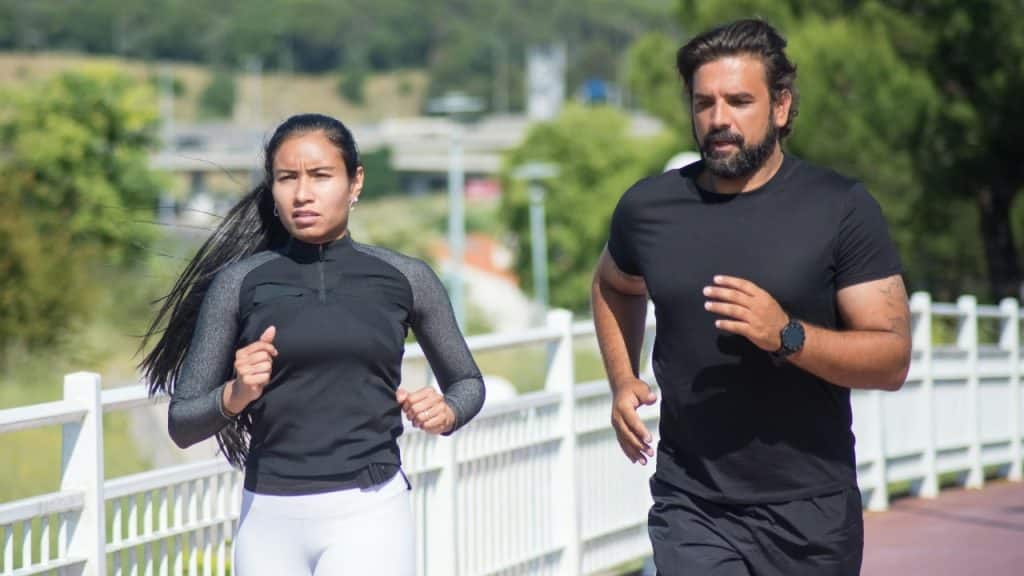A man and a woman in athletic wear running together outdoors on a paved path.