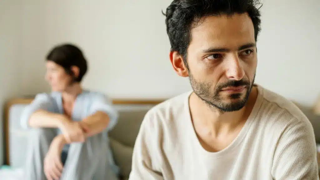 A man in a white shirt looks away from a woman sitting in the background.