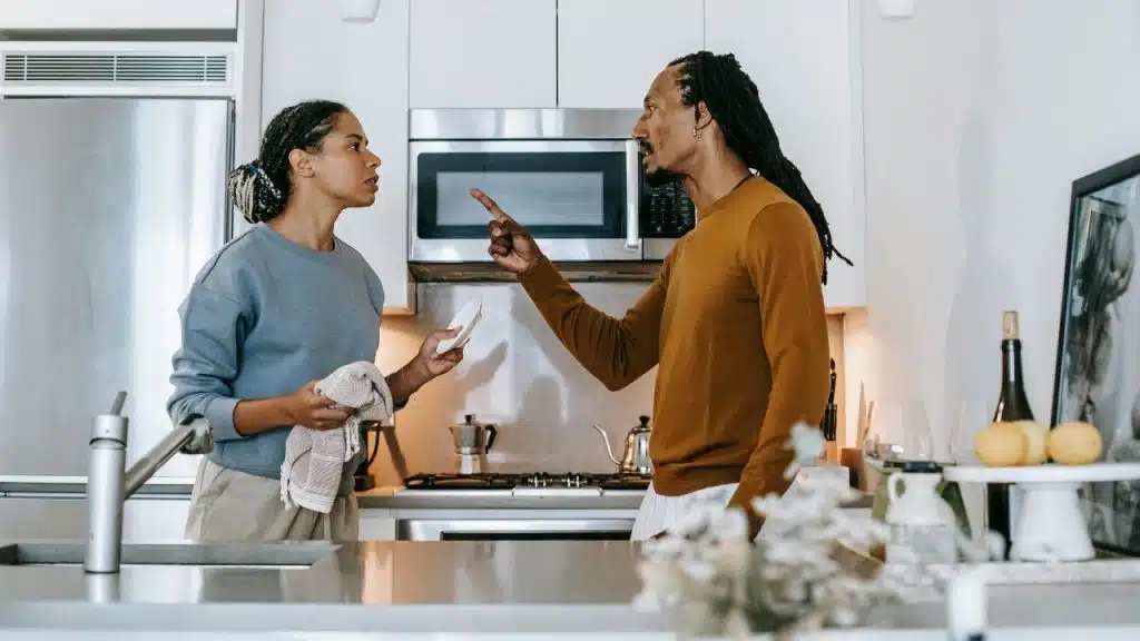 A man points a finger at a woman who is holding a white plate and cloth.