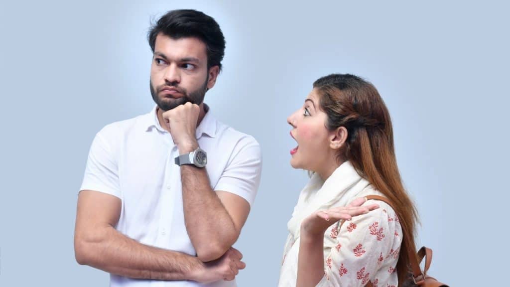 A man looks away thoughtfully while a woman beside him speaks with an expressive gesture.