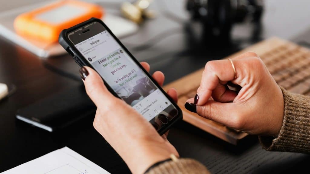 A person holds a smartphone displaying an Instagram post with text on a dark desk.